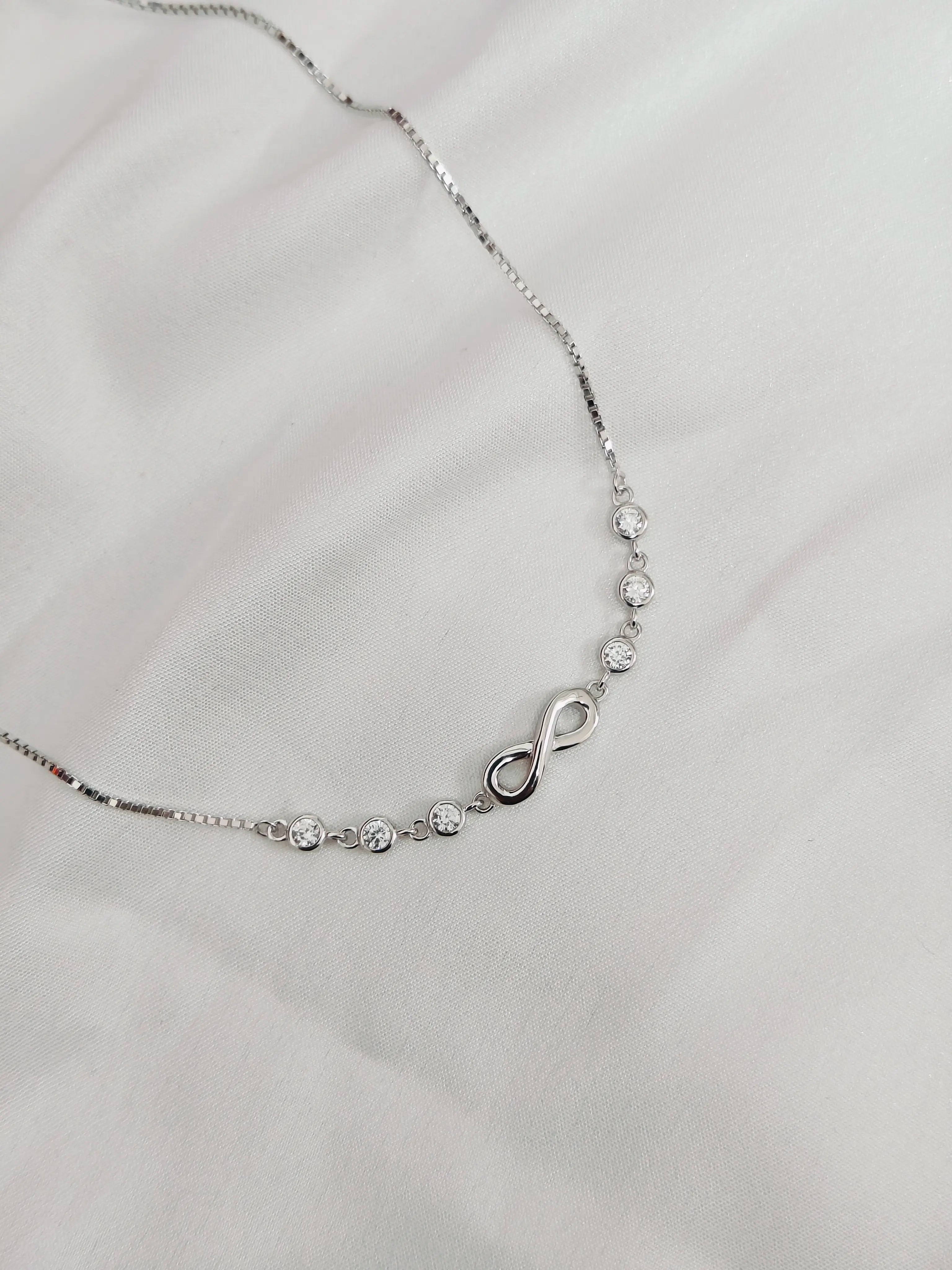 Silver necklace with a heart and infinity symbol on a light gray background